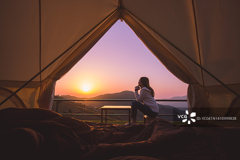 日出时在帐篷外微笑的女人，享受户外露营的放松和自由图片素材