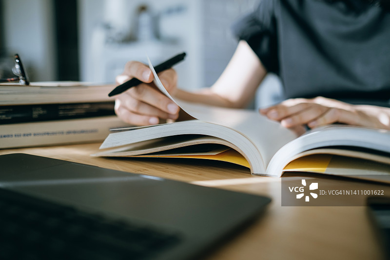 亚洲年轻女子在家读书并做笔记（特写）图片素材