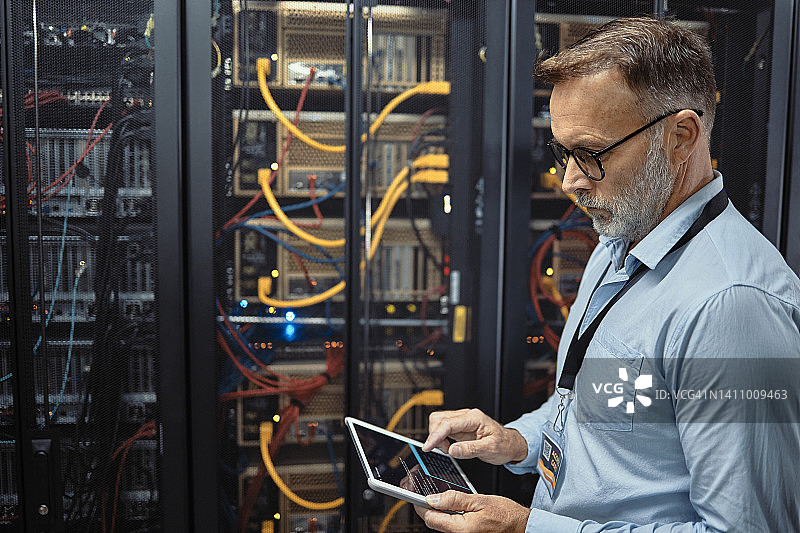 技师在服务器机房工作时使用平板电脑，成熟男人分析代码以修复计算机网络，同时在数据中心进行维护，工程师更新机器上的软件图片素材