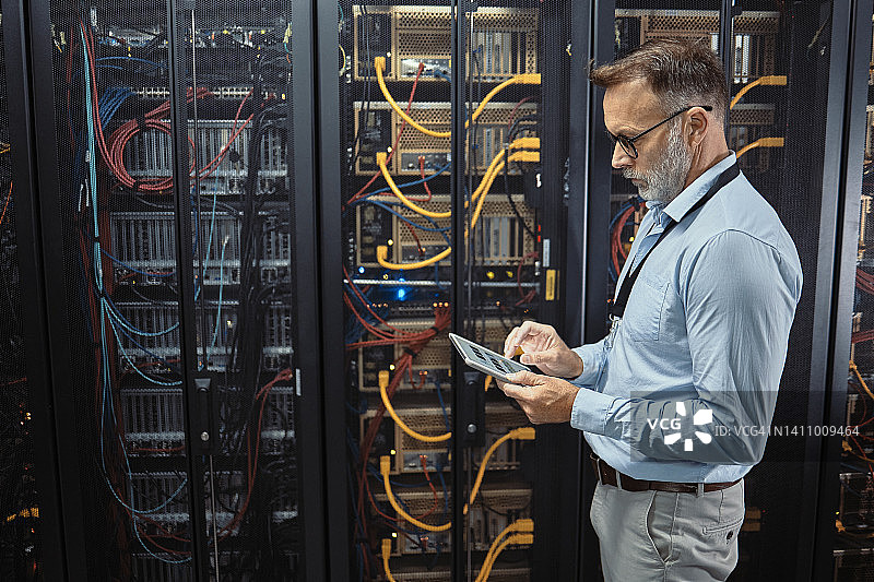 IT技术员在服务器机房使用数位板。成熟的程序员修复计算机系统和网络，同时在数据中心进行维护。工程师更新机器上的安全软件图片素材