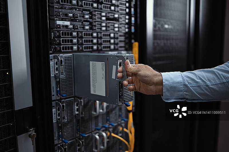 特写的手，一个IT专业人员从其外壳拆卸硬盘驱动器，而在服务器室工作。男性计算机工程师，诊断和评估硬件问题和存储设备问题图片素材