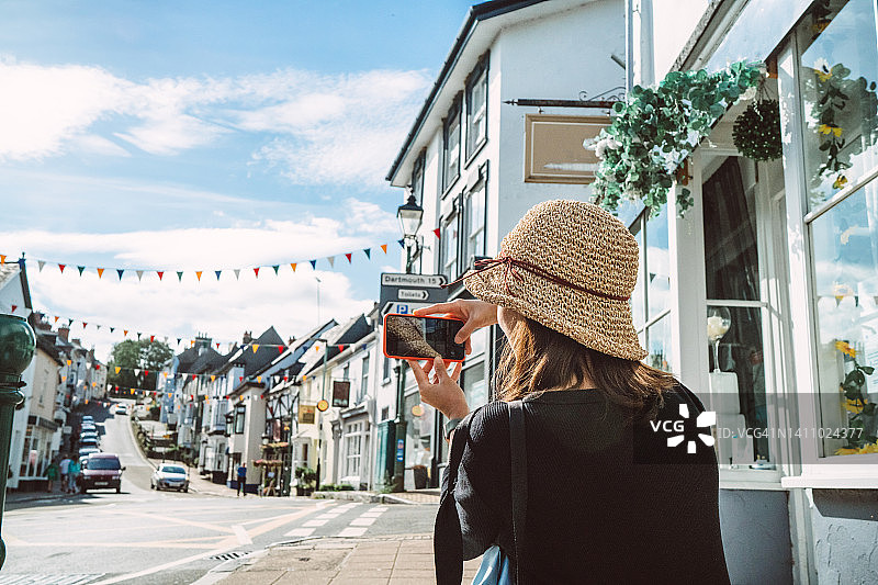 年轻女游客用手机拍摄美丽城镇风光的背影图片素材