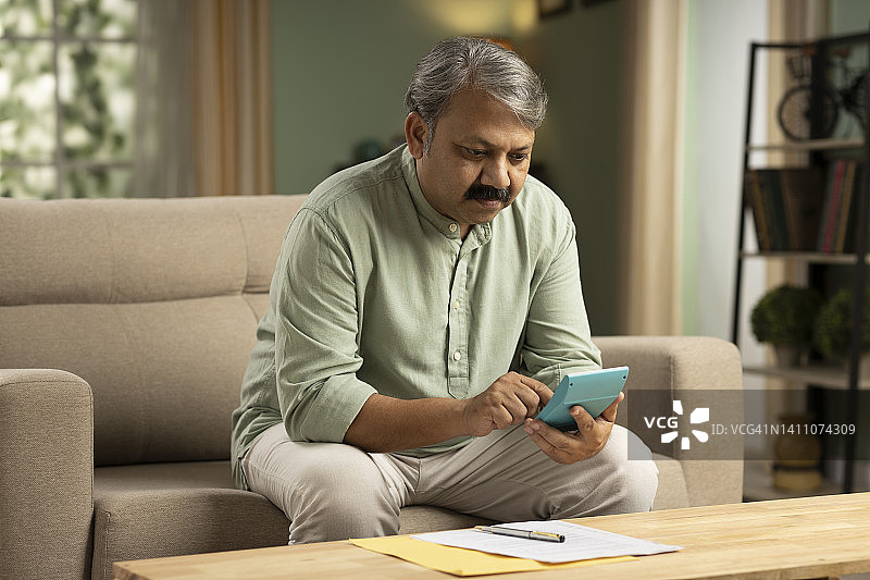 独自坐在沙发上计算财务的年长男人图片素材