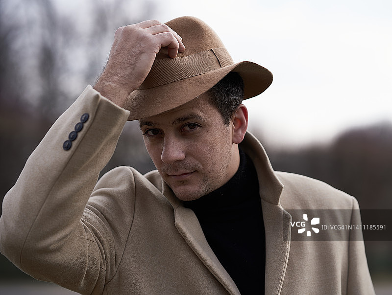 戴着米色帽子和穿着外套的深色头发男士在巴黎公园散步图片素材