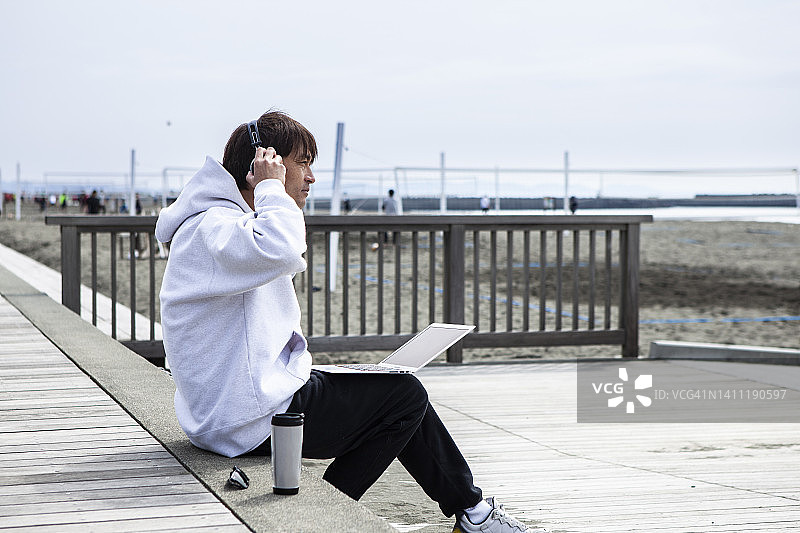 男人坐在海滩边用笔记本电脑工作图片素材