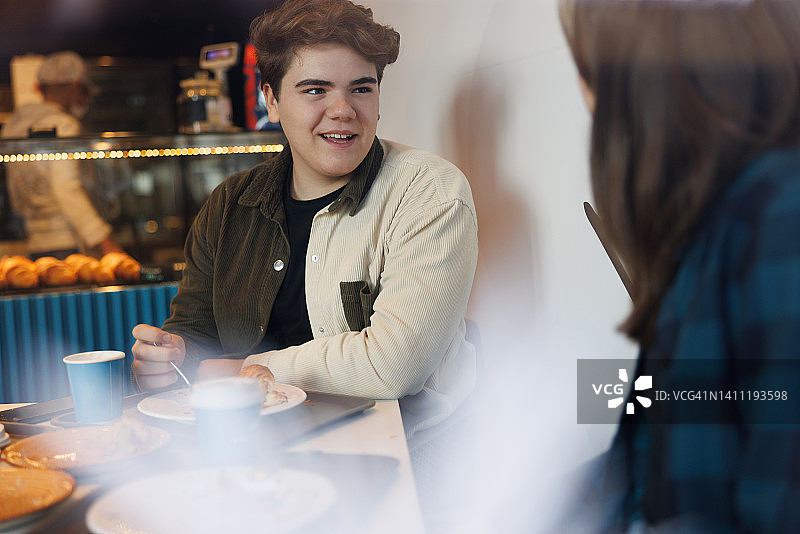 青少年在自助餐厅与女性朋友愉快交谈并享用茶点图片素材