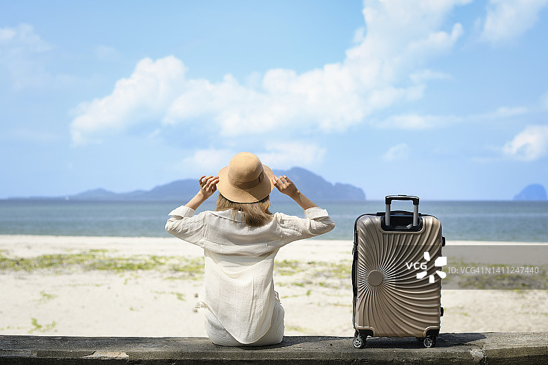 女子坐在海滩上，身旁放着行李图片素材