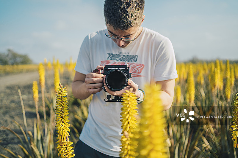 年轻男人用中画幅相机拍摄黄色植物图片素材