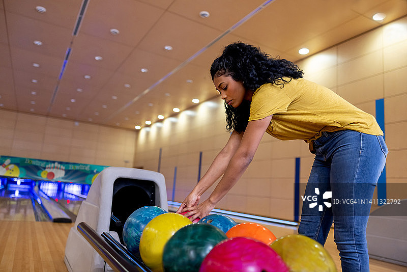 年轻女人打保龄球并捡起球图片素材