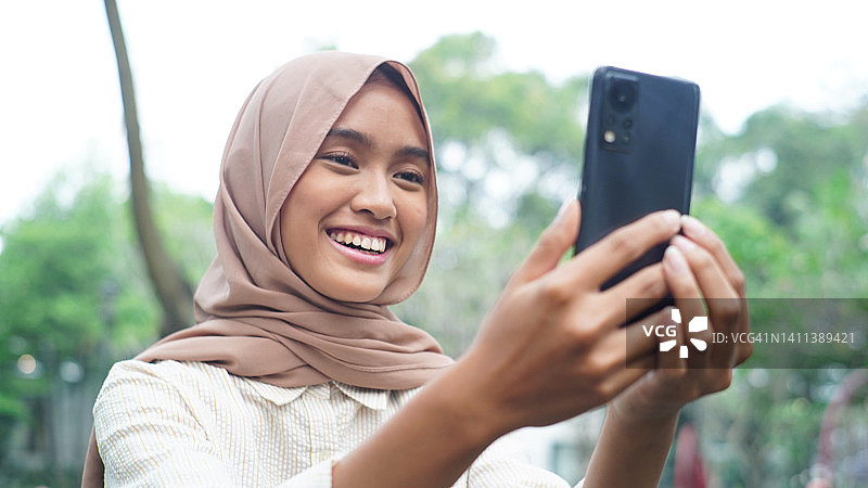 年轻女人在公园使用智能手机进行电话会议图片素材