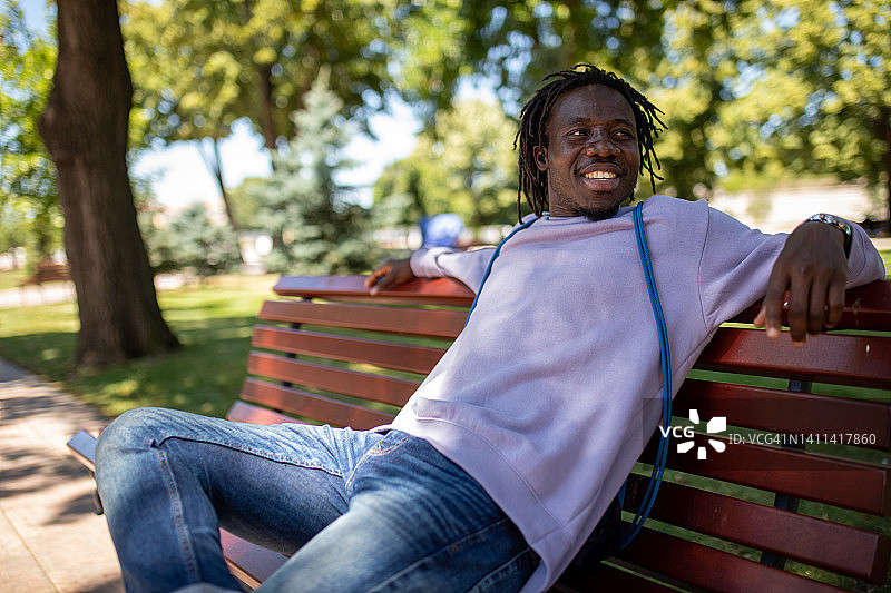 坐在公园长椅上的年轻非裔美国男子图片素材
