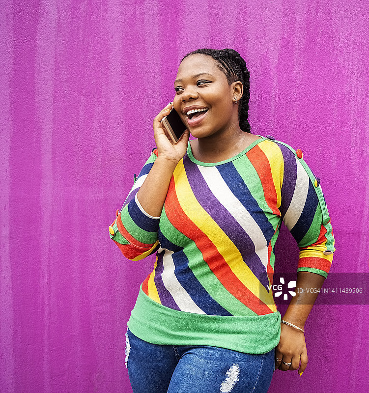 靠粉色墙壁打电话的年轻微笑女人图片素材