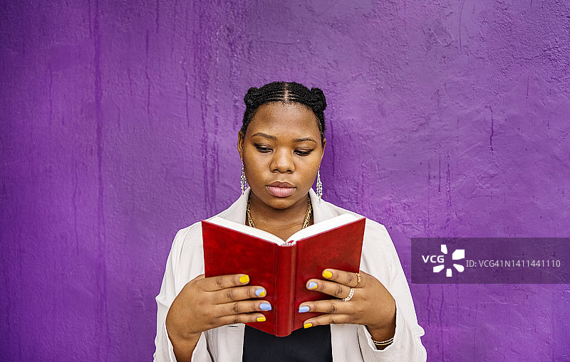年轻女人在紫色墙壁外阅读图片素材