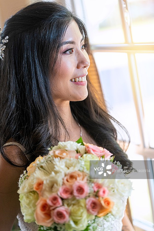 微笑的亚洲中年新娘手捧鲜花在窗边摆姿势图片素材