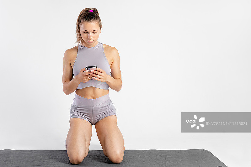 在工作室的运动女性肖像：健身锻炼概念，使用手机训练图片素材