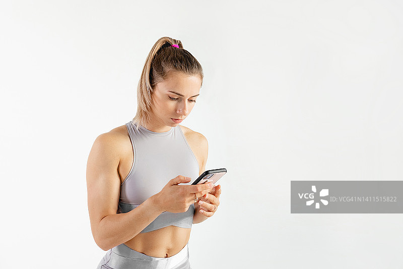 在工作室的运动女性肖像：健身锻炼概念，使用手机训练图片素材