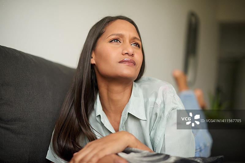 年轻的平静女人躺在沙发上，在家放松和沉思。女性在白日梦中回忆起遥远的记忆。一位女士在房子里的沙发上休息时思考着一个决定图片素材