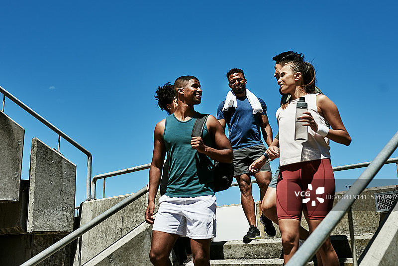 一群身材健美的年轻人穿着运动服从健身房走下楼梯，讨论新的锻炼或运动。图片素材