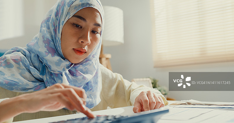 戴着头巾的年轻亚洲穆斯林女性使用计算器计算信用卡账单和每月支出图片素材