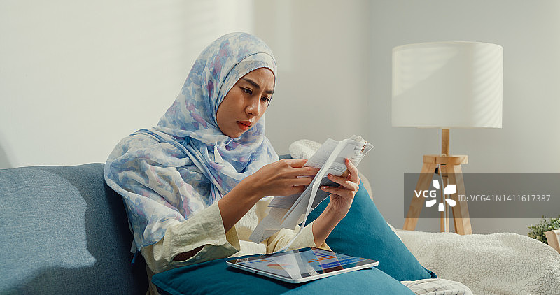 戴着头巾的年轻亚洲穆斯林女性使用平板电脑计算器，关注账单，计算信用卡收据，每月支出账单特写图片素材