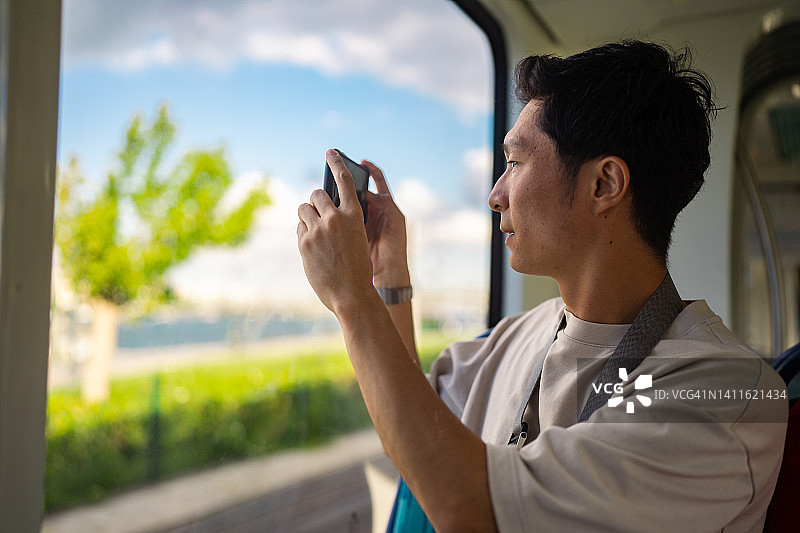 年轻男游客乘坐火车，拍摄沿途风景图片素材