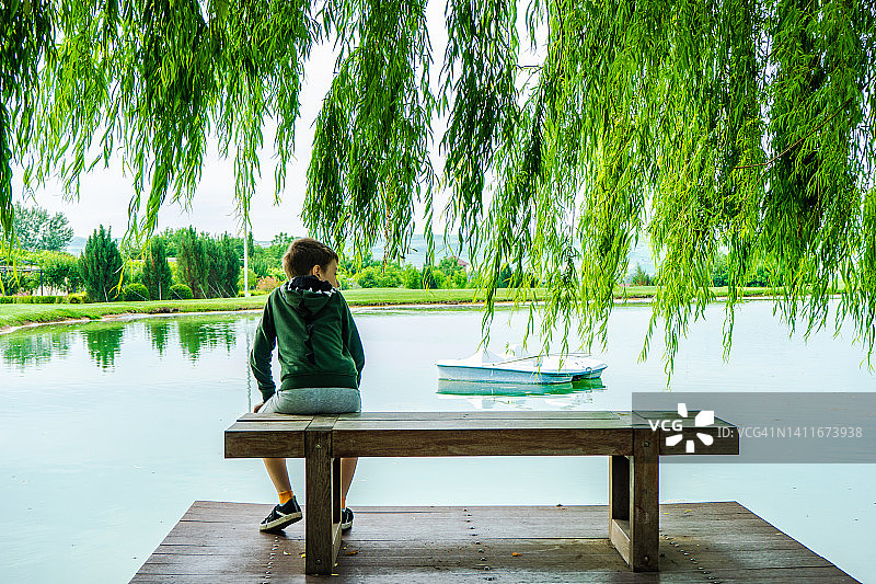 男孩坐在佐治亚州湖边的长椅上看风景的背影图片素材