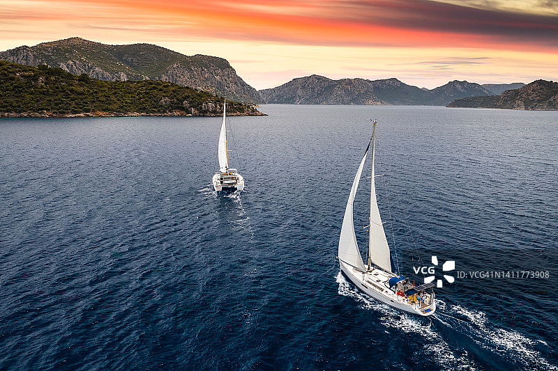日落时分，海上扬着白色风帆的游艇。在克罗地亚享受海上奢华假期，体验游艇之旅。图片素材