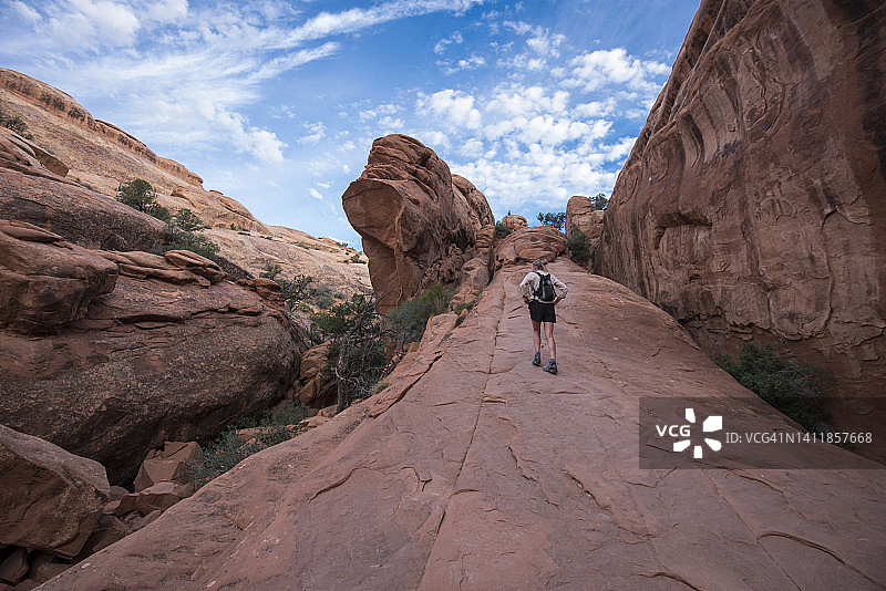 一个人在犹他州摩押附近的拱门国家公园攀登陡峭的岩石图片素材