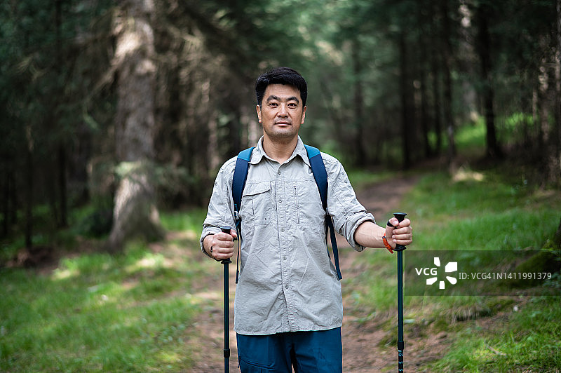 背着背包在森林小路上徒步的亚洲中年男人图片素材