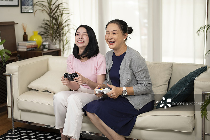 一位年长的母亲和她成年的女儿在家里的客厅里一起玩电子游戏图片素材