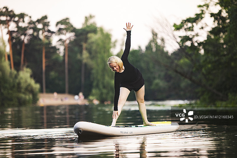 日落时分在桨板上练习瑜伽的年轻女人图片素材