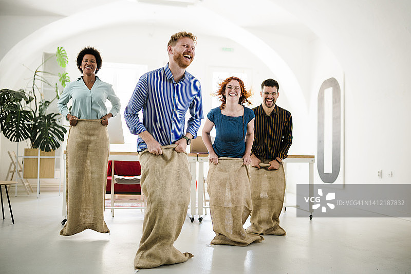 一群快乐的企业家在办公室里玩麻袋赛跑图片素材