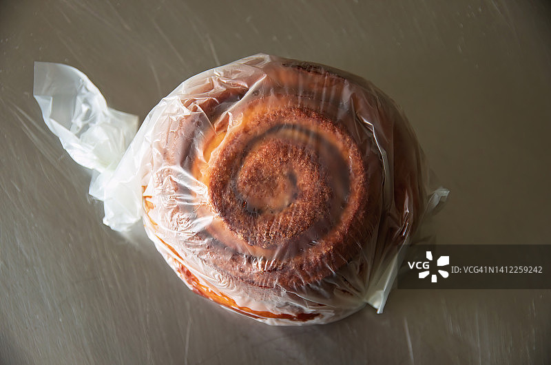 不锈钢台面上塑料包裹的肉桂卷甜面包图片素材