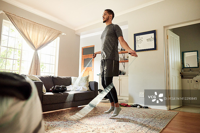 年轻男子在家锻炼时在客厅里跳绳图片素材