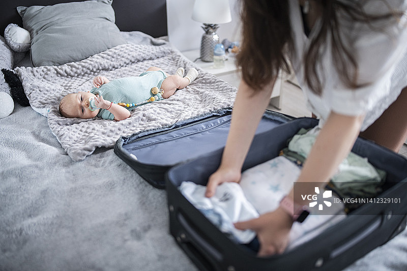 母亲将婴儿服装装在手提箱里图片素材