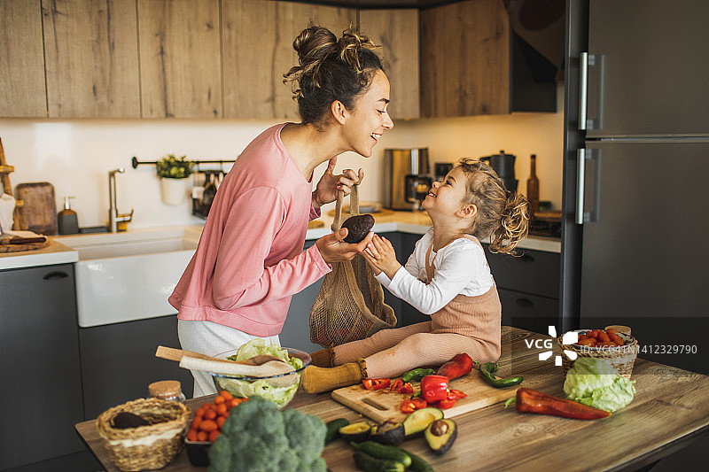 快乐的母亲用牛油果和女儿玩耍，可持续育儿图片素材