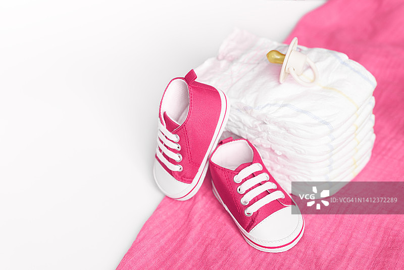 粉色餐巾上的尿布堆、婴儿运动鞋和奶嘴图片素材
