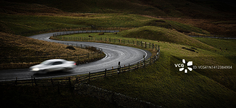 在英国德比郡峰区国家公园蜿蜒道路上行驶的银色跑车图片素材