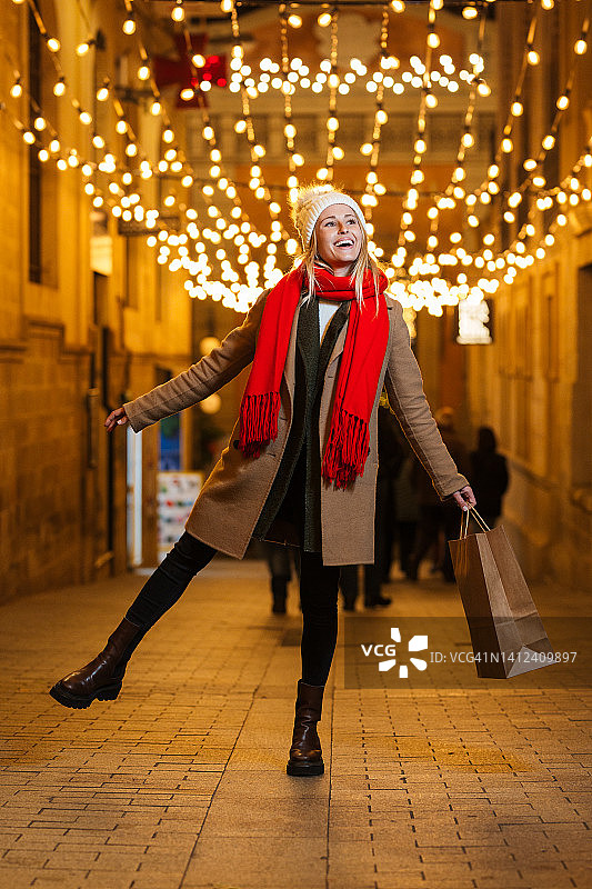 可爱的女人提着购物袋走在街头市场，看着商店和仓库的窗户图片素材