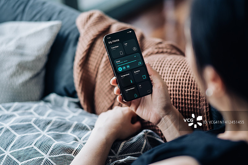 年轻亚洲女性使用智能手机设置智能家居系统图片素材