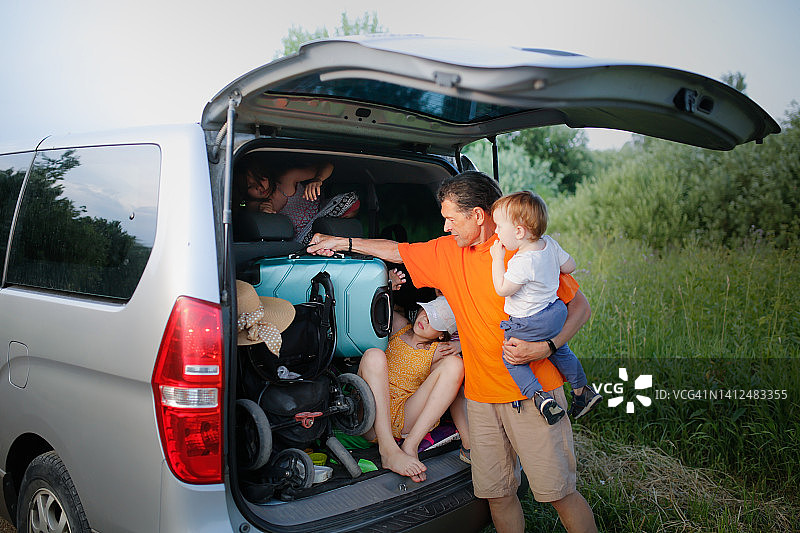 有趣的姐妹在后备箱里玩耍，爸爸和孩子把手提箱装进车里图片素材