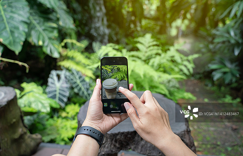 在咖啡店花园用智能手机拍咖啡杯的女人图片素材