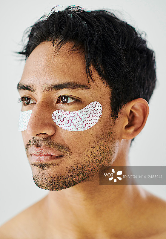 使用眼部、面部和皮肤护理贴的男人，工作室背景。男性眼部或面颊的抗衰老胶原蛋白贴片，使皮肤更年轻、清新和清洁。男性面部护理程序图片素材