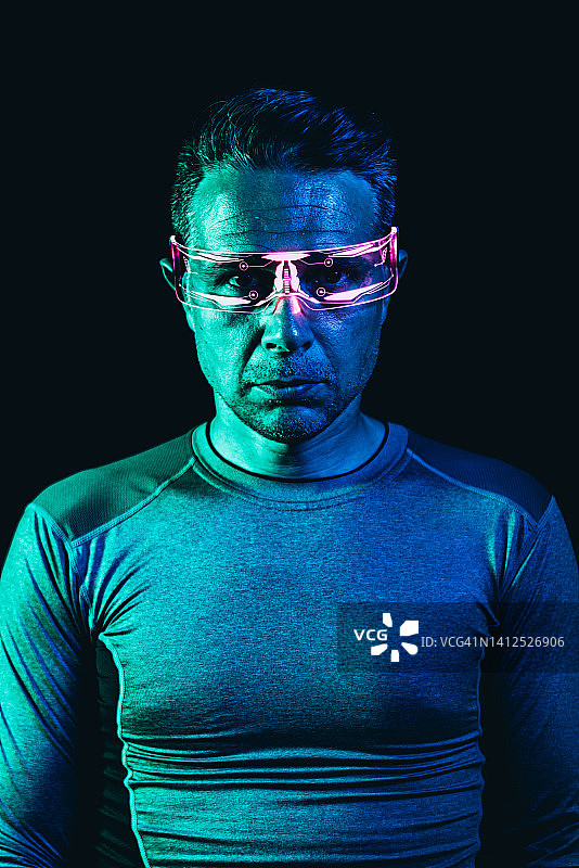 佩戴粉色灯光网络眼镜，身穿灰色紧身T恤的男人肖像，蓝色环境，黑色背景。机器人，赛博格，未来和元宇宙概念图片素材