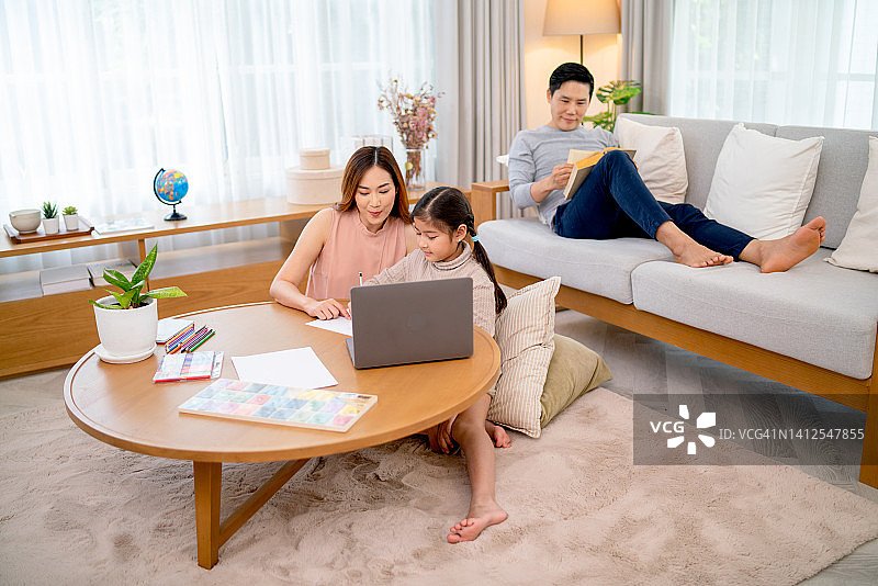 亚洲母亲在客厅帮助女儿进行在线学习图片素材