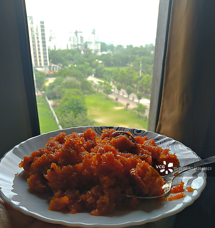 女人手持陶瓷盘，展示自制胡萝卜甜点，窗边有城市景观图片素材