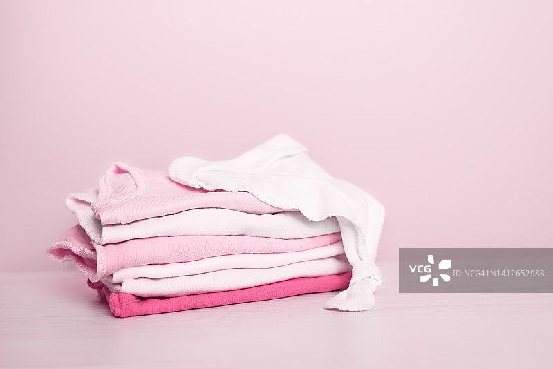 粉色背景上的新生婴儿干净衣物堆叠特写，留有文字空间，婴儿期和母性概念图片素材