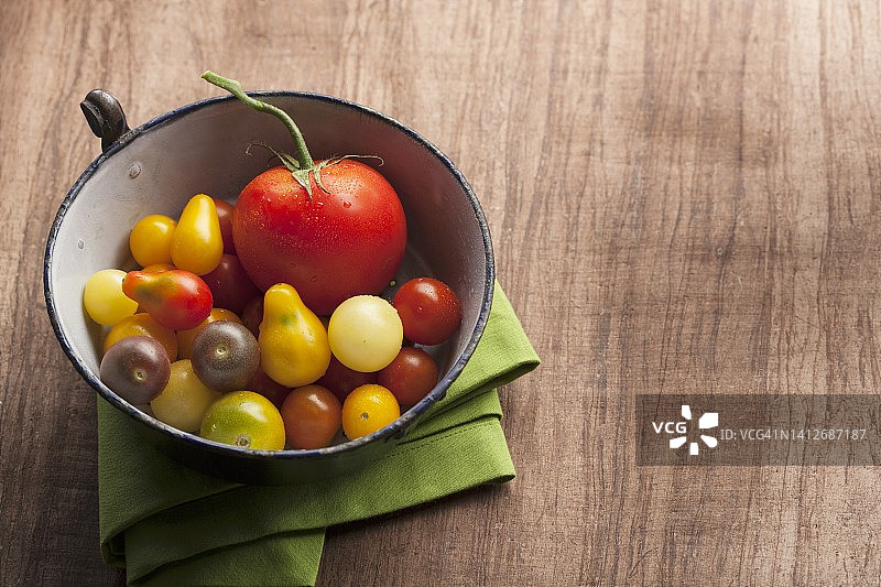 木质背景上，古董搪瓷碗里的各色番茄和绿色餐巾图片素材