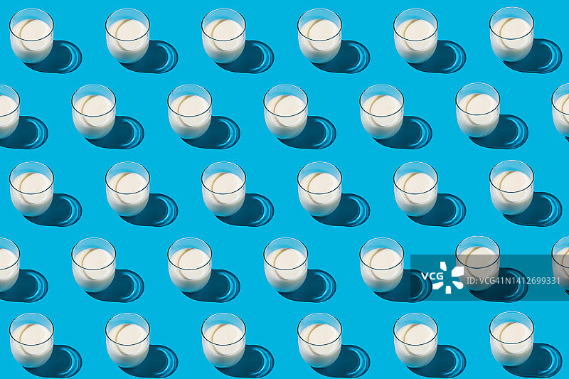 蓝色背景下，装满牛奶的玻璃杯在强光下的图案。乳制品、短缺、钙、成长和饮用概念图片素材