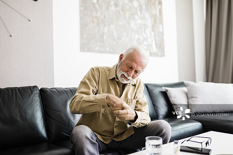 坐在沙发上因关节炎而手部不适的年长男人图片素材